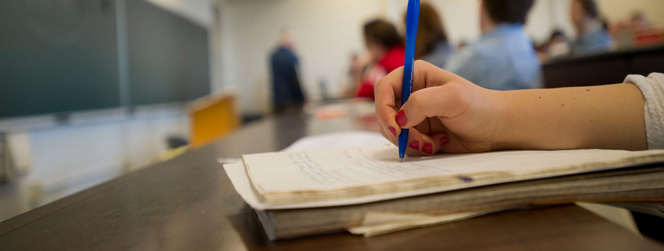 A hand holding a pen to a notebook ready to take notes.