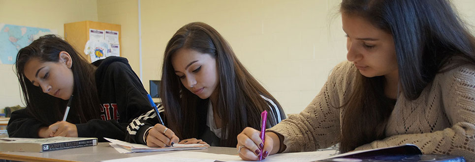 Three female students writing a test in a classroom.